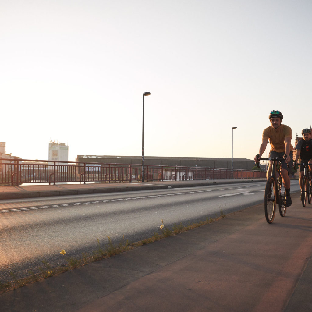 Zwei Radfahrer fahren bei Sonnenaufgang oder Sonnenuntergang auf einer Brücke.