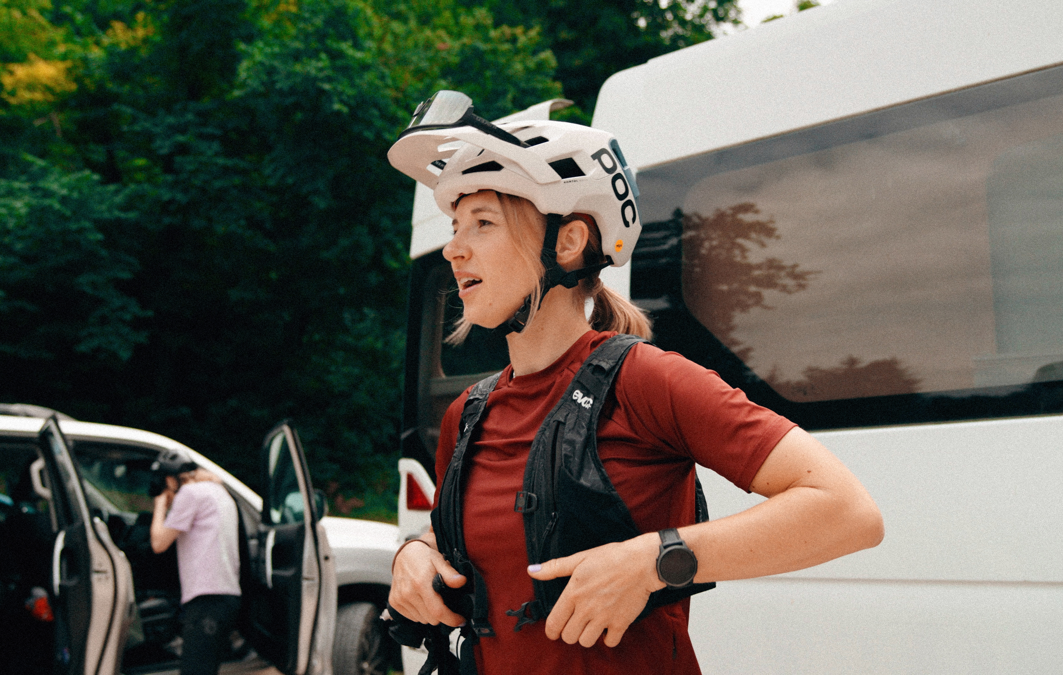 Eine Radfahrerin mit Helm steht vor einem weißen Van und zieht ihre Weste zurecht.