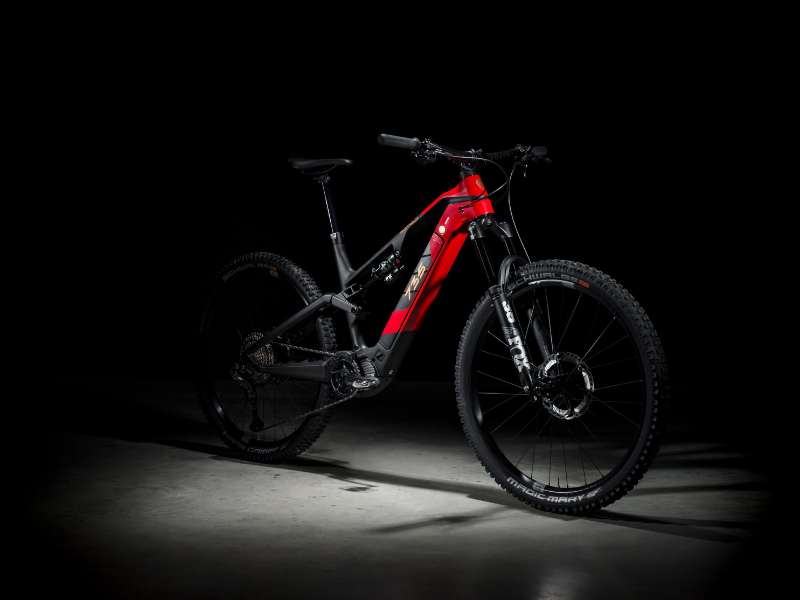 Ein rot-schwarzes E-Mountainbike steht im Scheinwerferlicht vor dunklem Hintergrund.