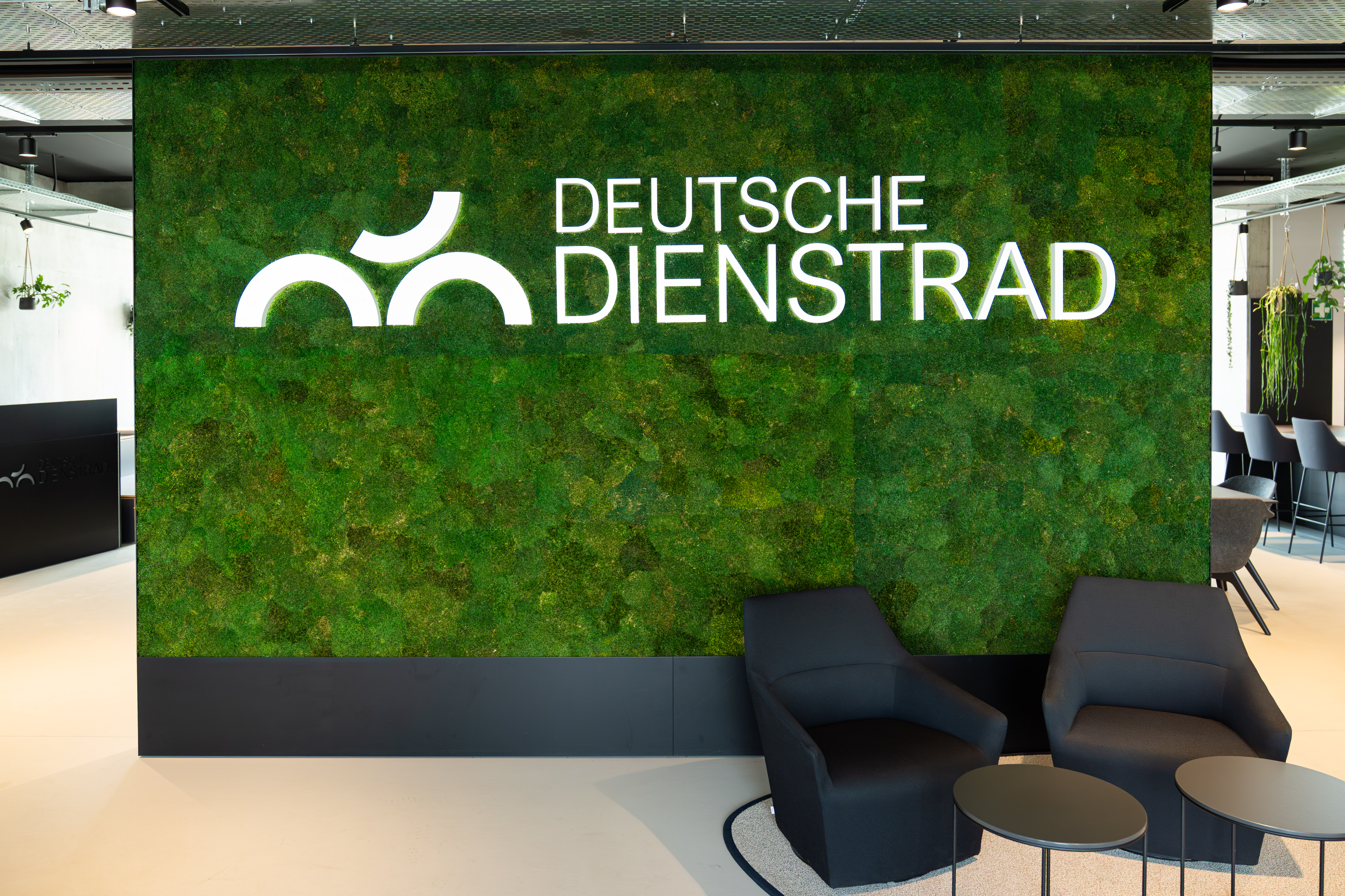 Begrünte Wand mit dem Schriftzug „DEUTSCHE DIENSTRAD“ in einem modernen Büro-Loungebereich mit Sesseln und kleinen Tischen.