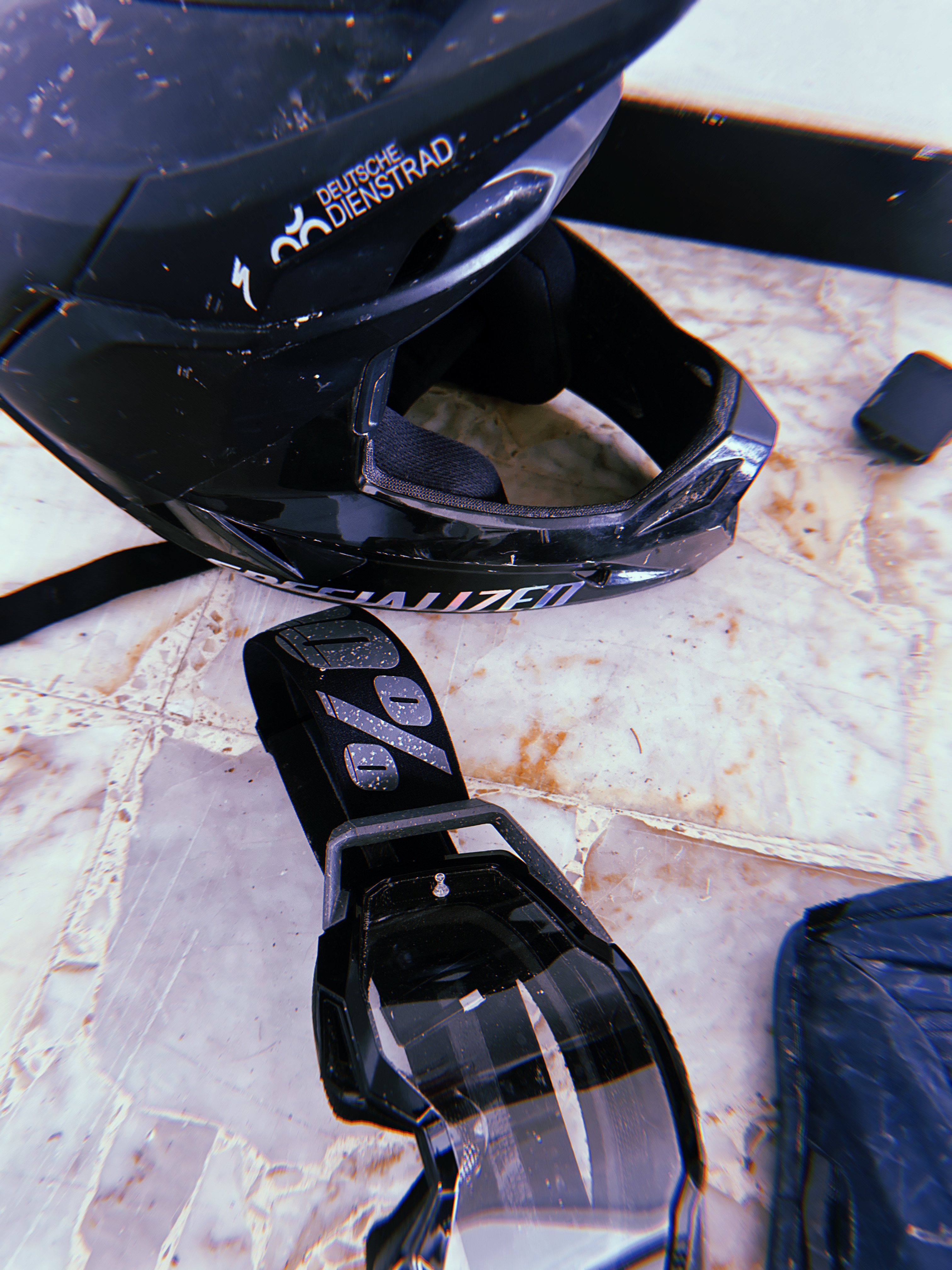 Nahaufnahme eines schwarzen Fullface-Mountainbikehelms mit „Deutsche Dienstrad“-Logo neben einem schwarzen Funkgerät auf einer hellen Steinfläche.