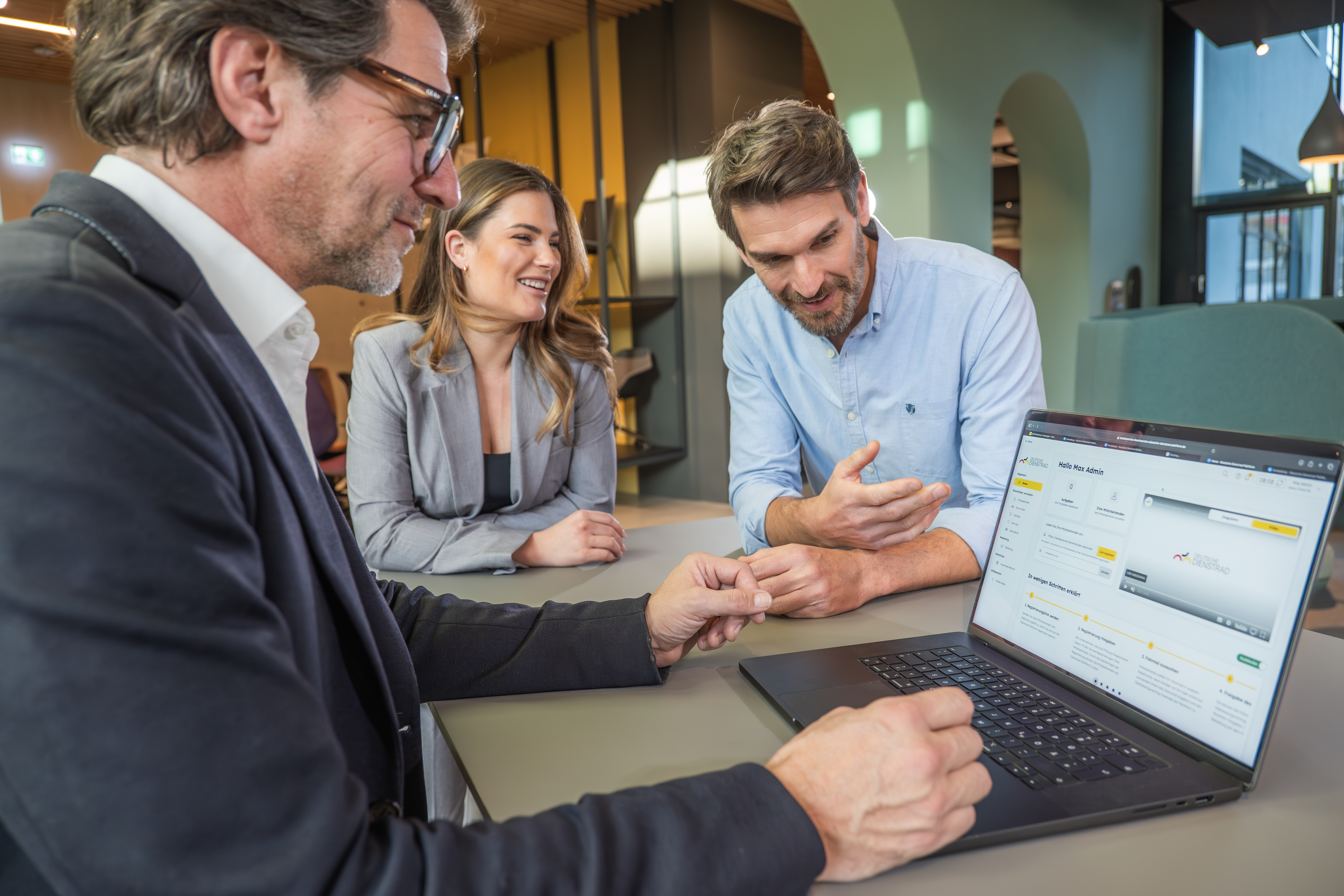 Drei Personen besprechen gemeinsam Inhalte auf einem Laptop in einer modernen Büroumgebung.